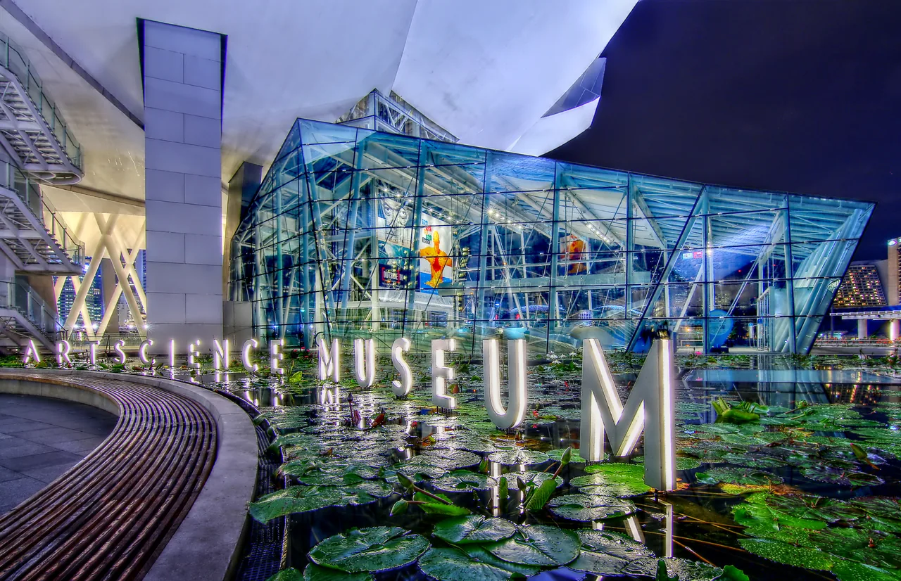 The ArtScience Museum's glass entrance and sign lit up above the lily pond at night