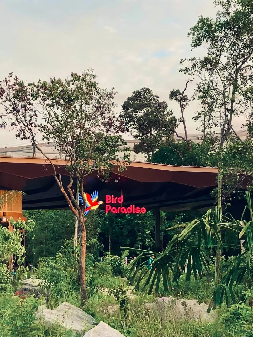 Area Bird Paradise yang hijau dan rimbun dikelilingi pepohonan, dengan papan nama pintu masuk