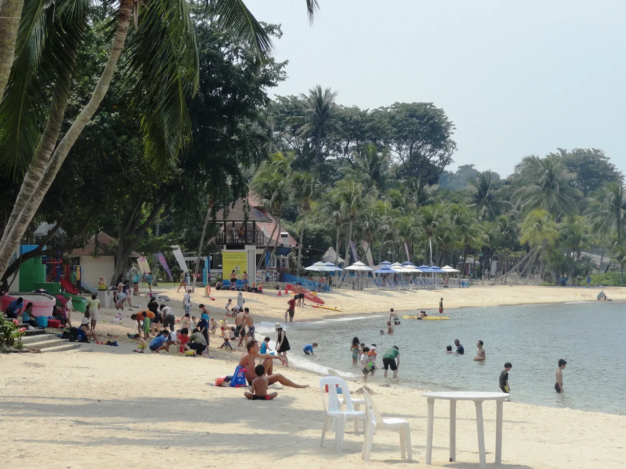 A sandy beach with palm trees and visitors on Sentosa Island, Singapore