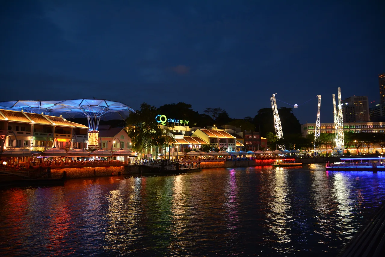 Clarke Quay riverside in Singapore lit up with colourful lights at night, with bumboats on the Singapore River