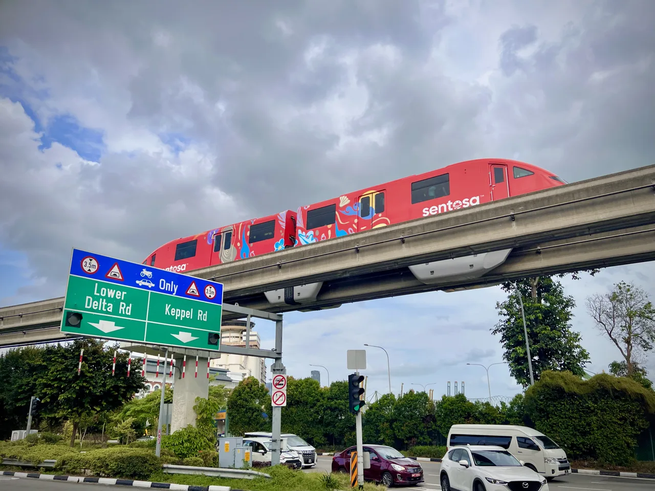A red Sentosa Express monorail car crossing an elevated guideway above a road