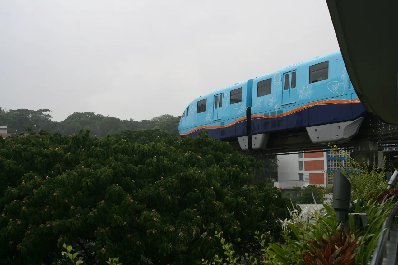 A blue Sentosa Express monorail train on an elevated track above dense green trees