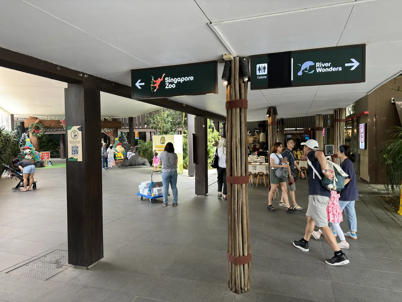 Overhead signs at Mandai Wildlife EAST pointing left to Singapore Zoo and right to River Wonders, with visitors walking past
