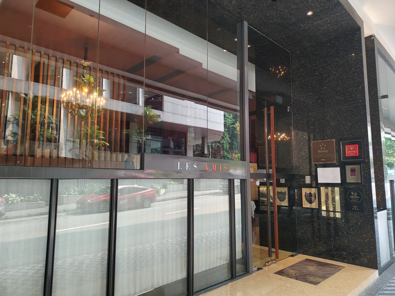 The glass entrance of Les Amis on Scotts Road with its name above the door and award plaques on the wall beside it