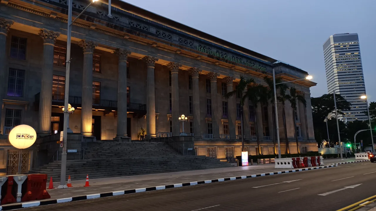 The colonnade of the former City Hall at dusk with the lit National Gallery Singapore sign above it