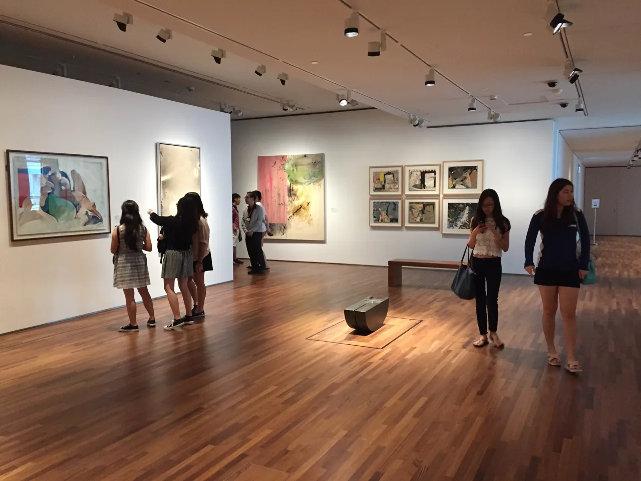 Visitors looking at paintings in a wood floored room of the DBS Singapore Gallery