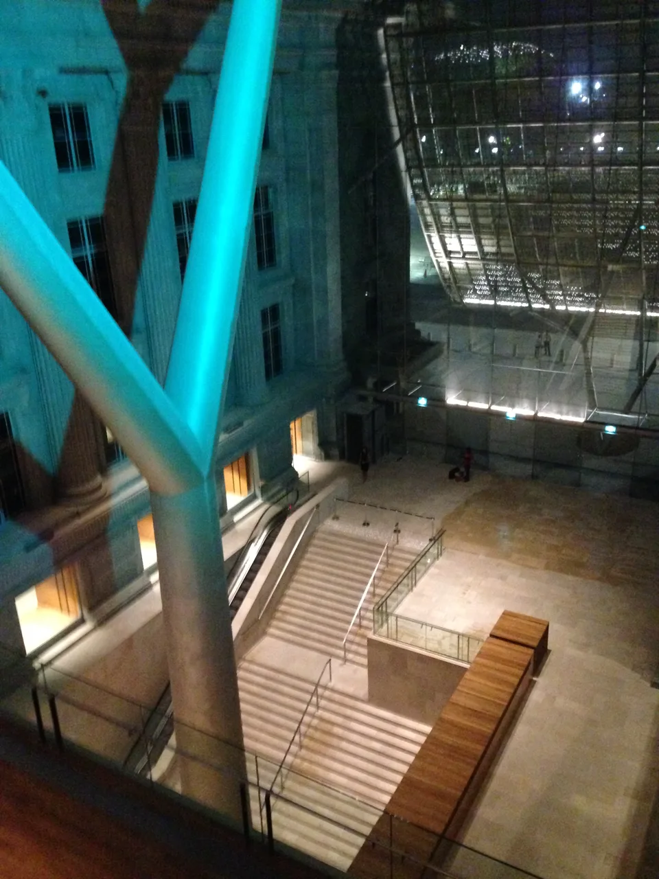 The Padang Atrium at night from an upper walkway, stairs below and the glass roof to the right