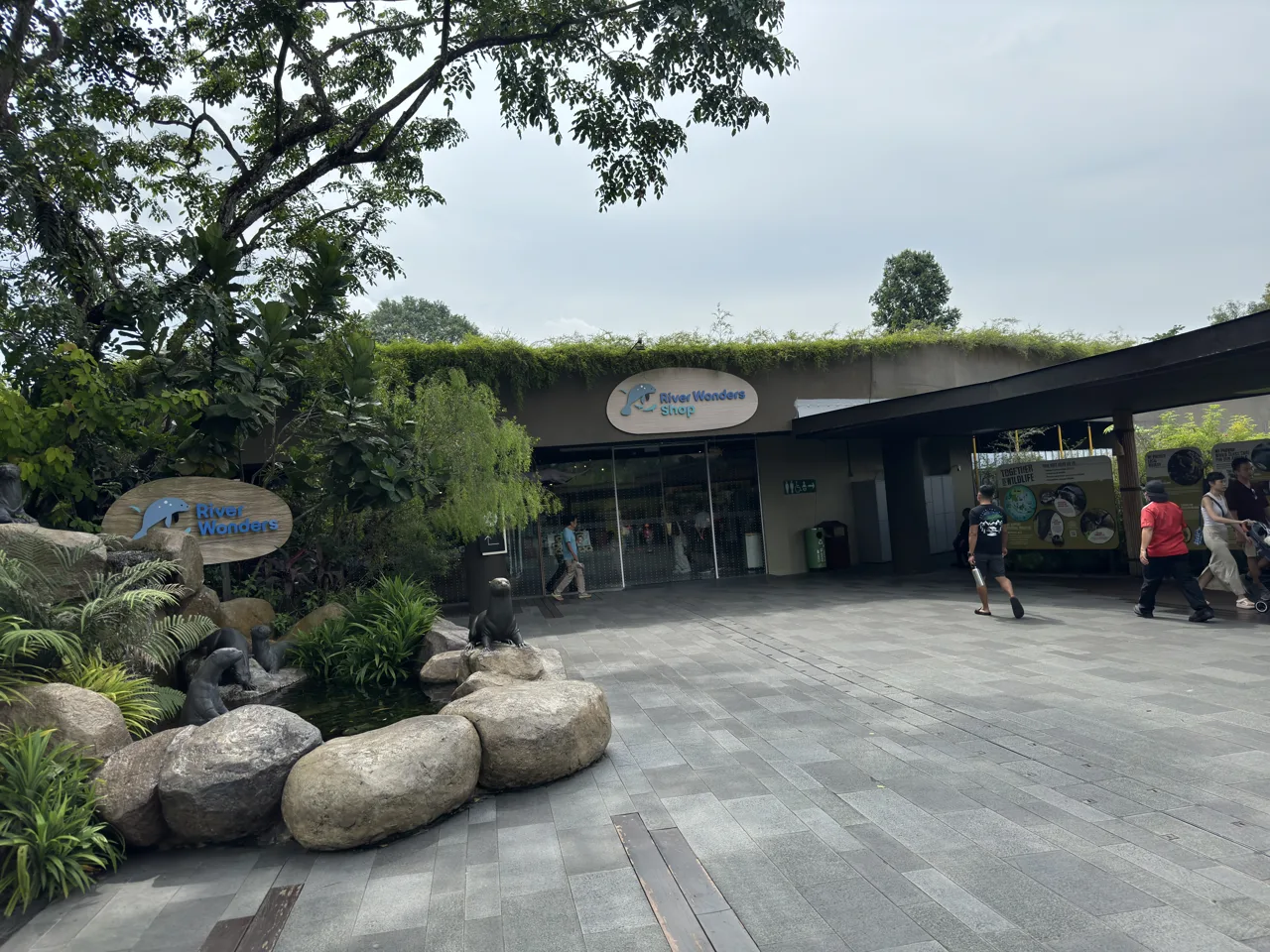 Signage and the shop building at the River Wonders entrance plaza, with visitors walking past