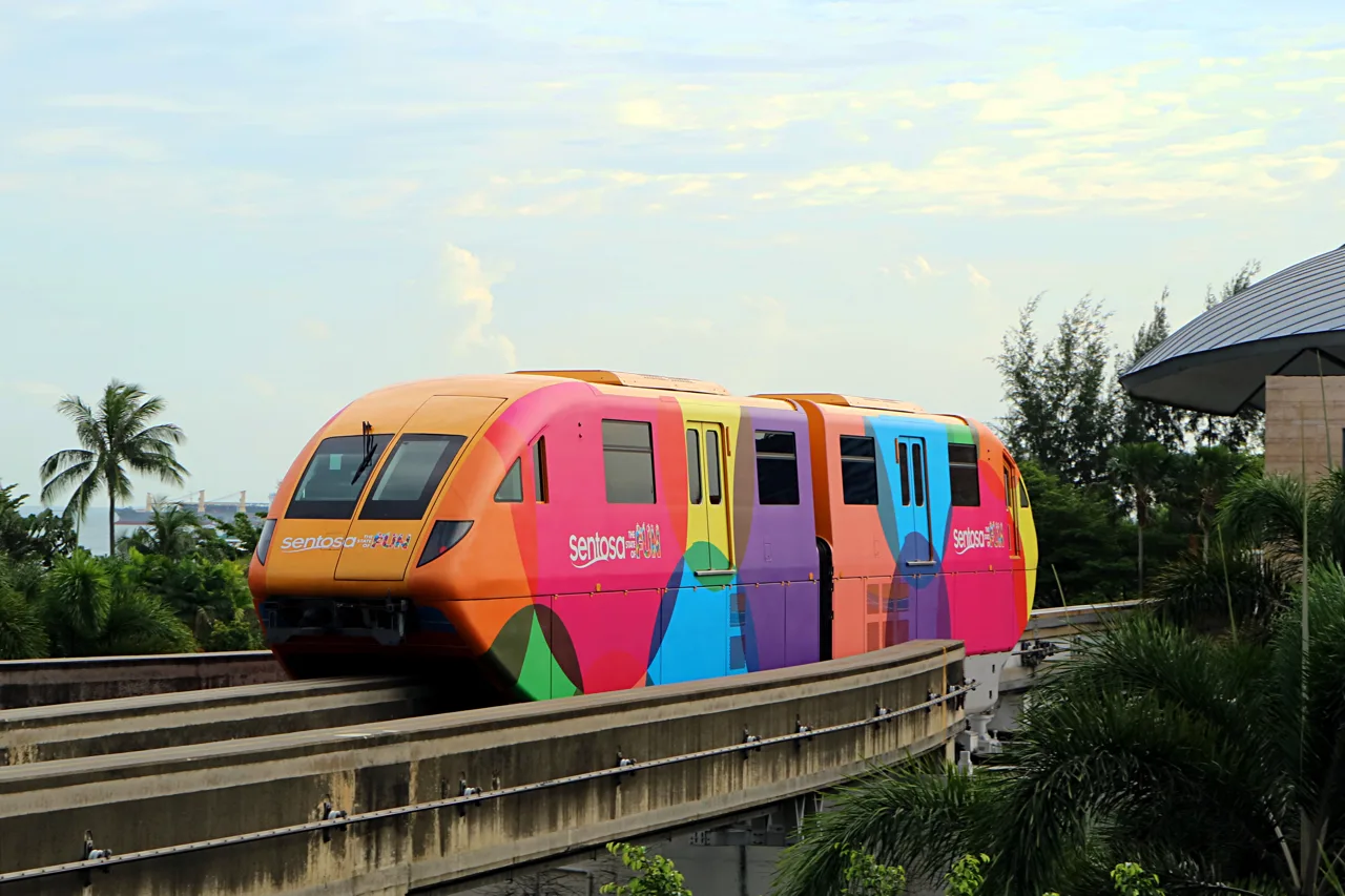 A brightly liveried Sentosa Express monorail car running along the elevated track above trees