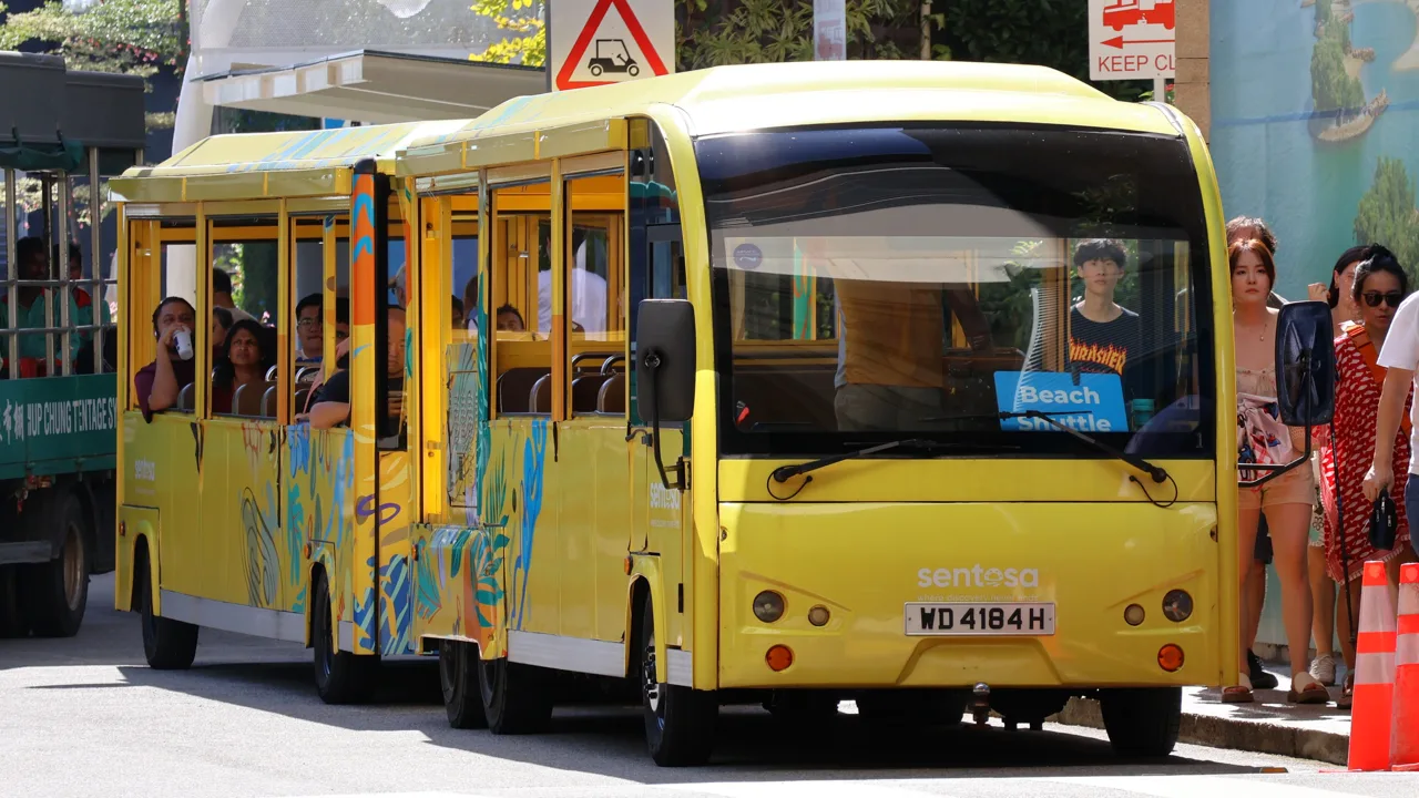 A yellow Beach Shuttle tram at a stop with passengers waiting beside it