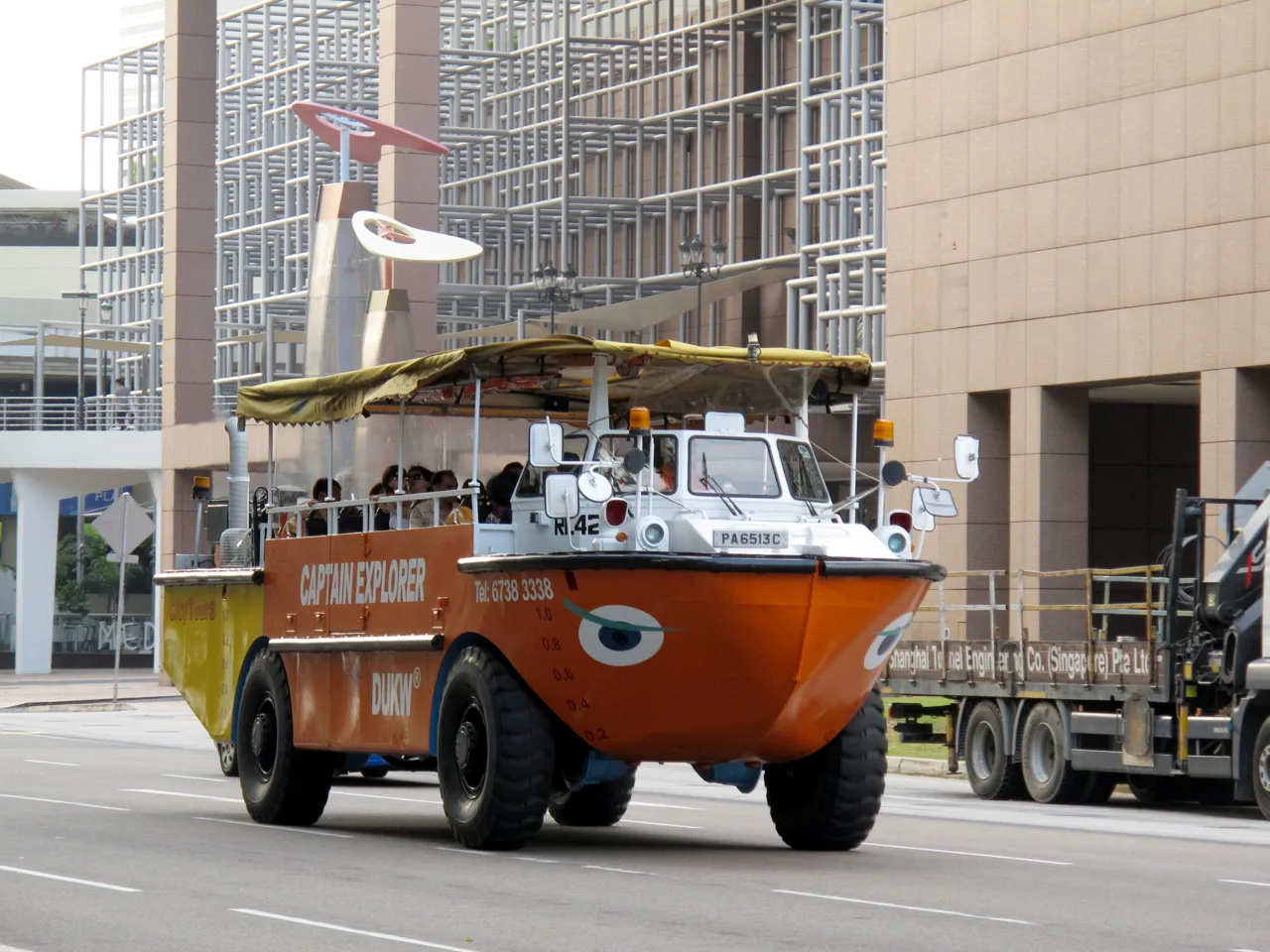 An orange amphibious vehicle lettered Captain Explorer DUKW with a boat-shaped bow driving through central Singapore