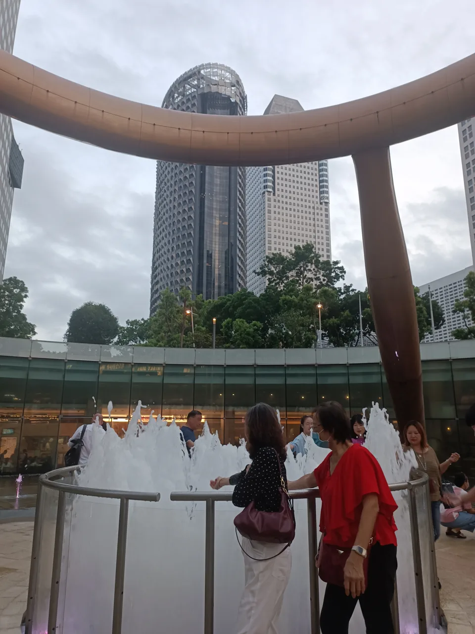 The Fountain of Wealth at Suntec City running beneath its large bronze ring with visitors at the railing and office towers behind