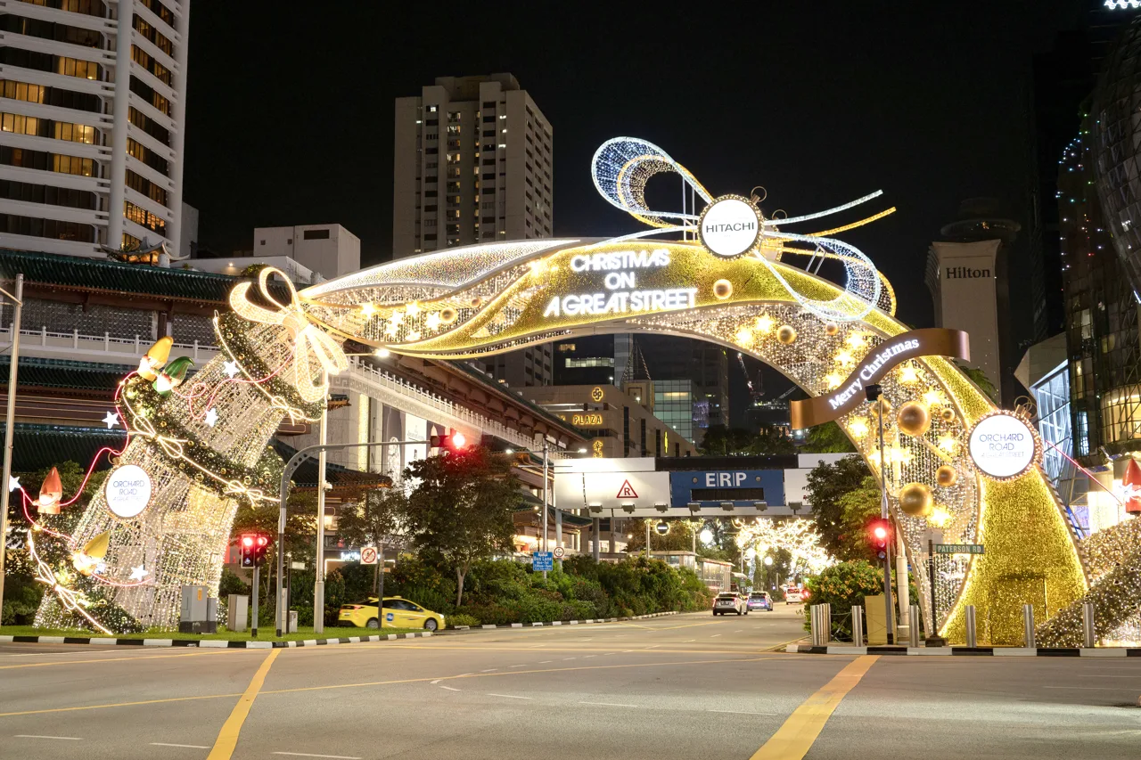 A lit archway over Orchard Road at night in gold and white with hotel towers behind it