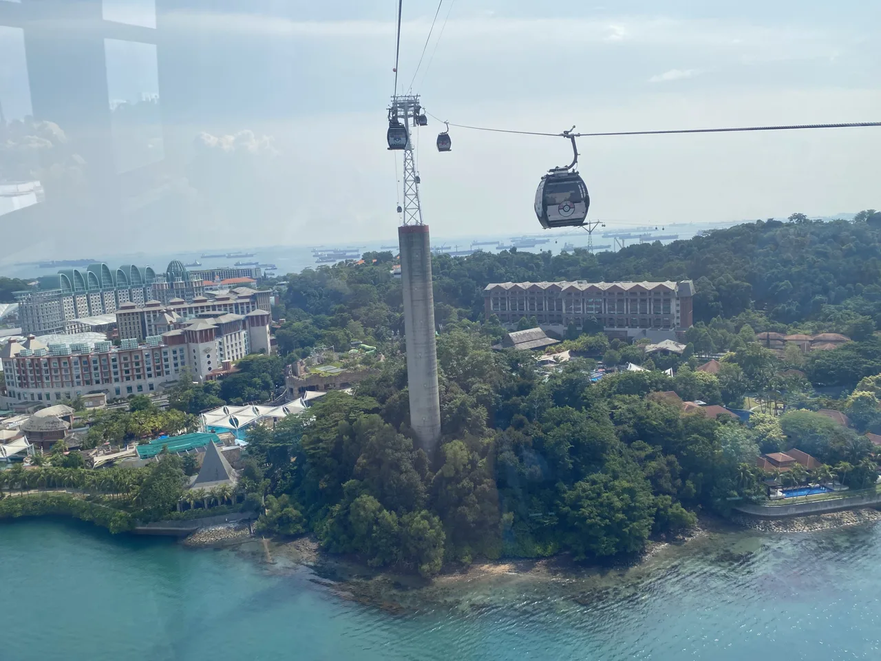 A Singapore Cable Car cabin on the Mount Faber Line crossing above Sentosa, with resort buildings and turquoise water below