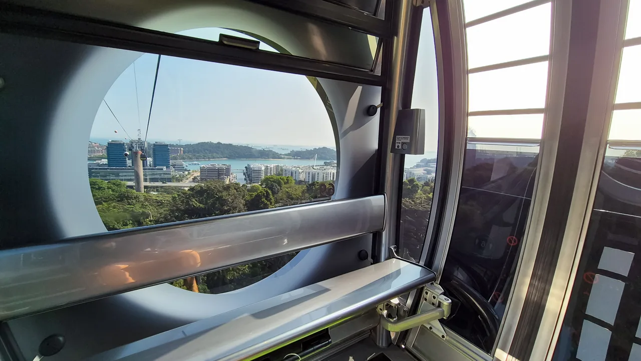 The view out through the curved glass of a Singapore Cable Car cabin towards the harbour