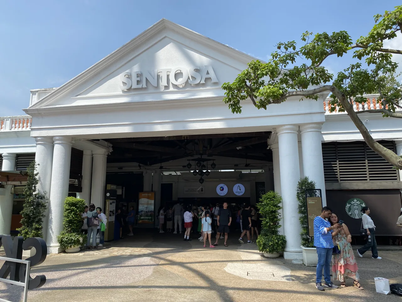The colonnaded Sentosa cable car station entrance with visitors walking in under the Sentosa sign