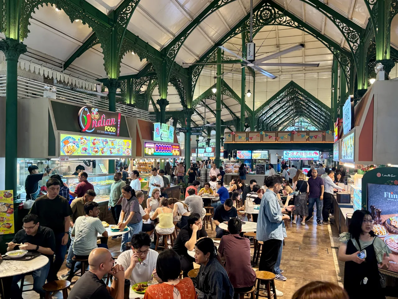 The interior of Lau Pa Sat hawker centre, with round tables and stools filled with diners under a green cast iron roof