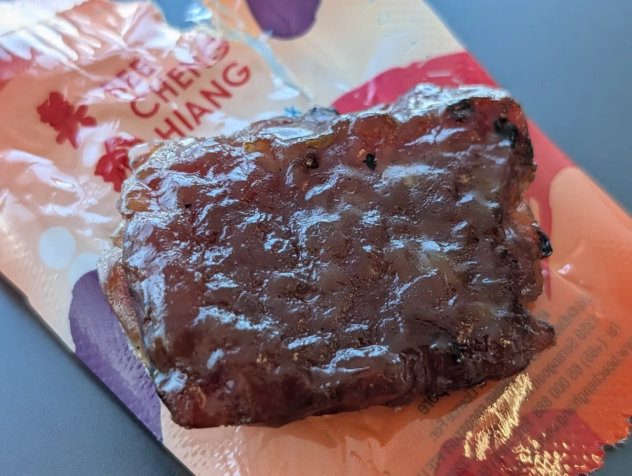 A single glazed slice of bak kwa resting on an opened Bee Cheng Hiang wrapper