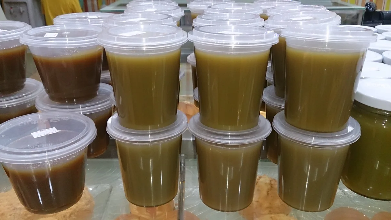 Stacked plastic tubs of kaya on a bakery counter, some green and some brown