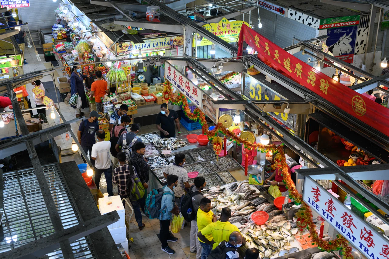 The wet market floor of Tekka Centre seen from the level above, with shoppers carrying bags between fish and meat counters