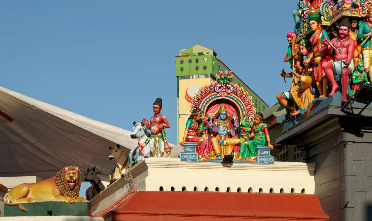 Painted figures and a lion statue along the roofline of Sri Mariamman Temple under a clear sky Painted figures and a lion statue along the roofline of Sri Mariamman Temple under a clear sky