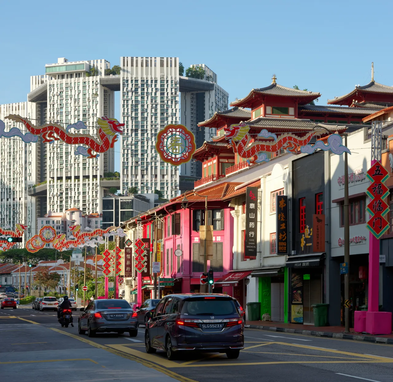 South Bridge Road in Chinatown by day, with dragon and lantern decorations strung above the road, shophouses on both sides and apartment towers behind