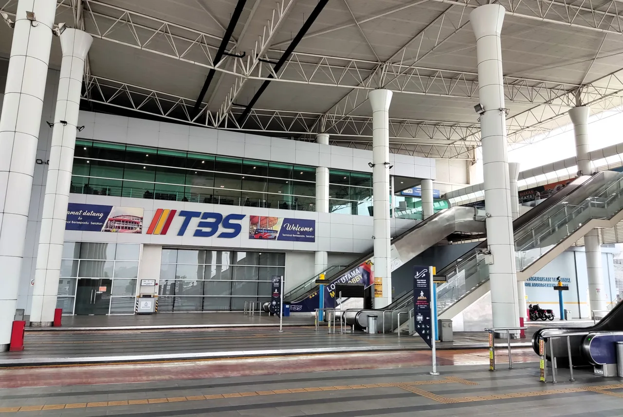 The arrival platform level at Terminal Bersepadu Selatan in Kuala Lumpur, with the TBS sign above the entrance and escalators to the station