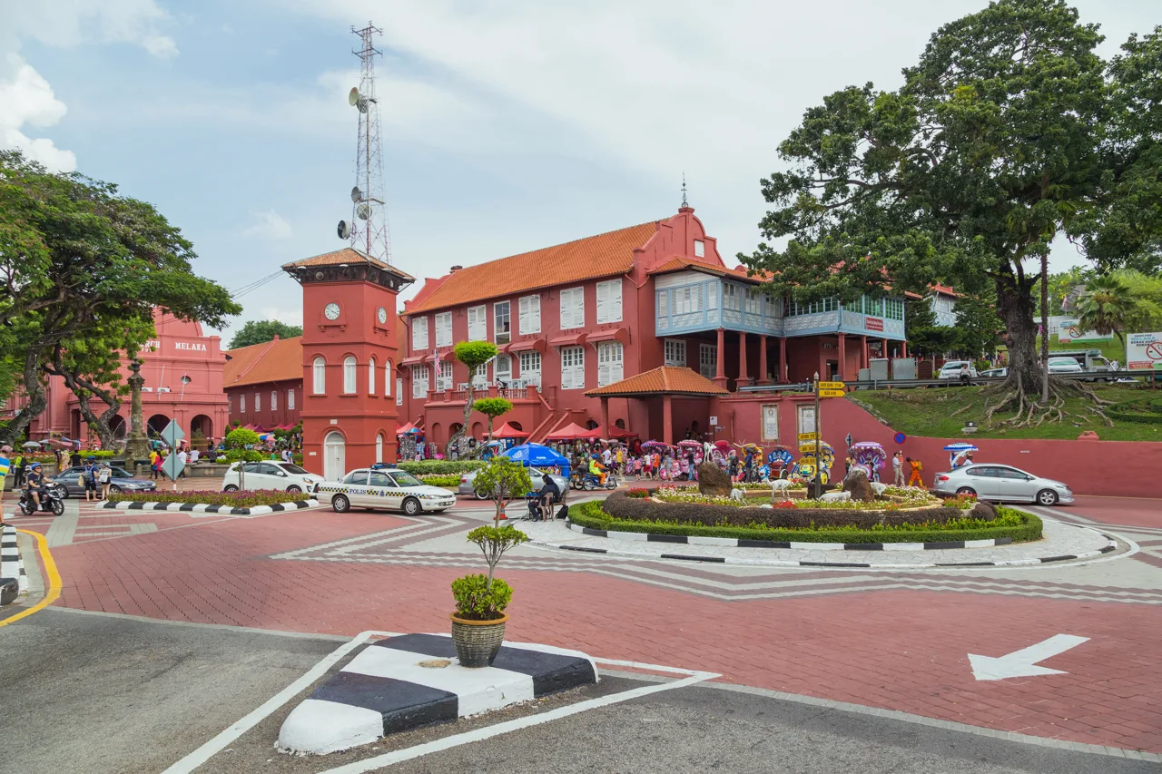The red Stadthuys building and clock tower on Dutch Square in Melaka, with decorated trishaws lined up to the right