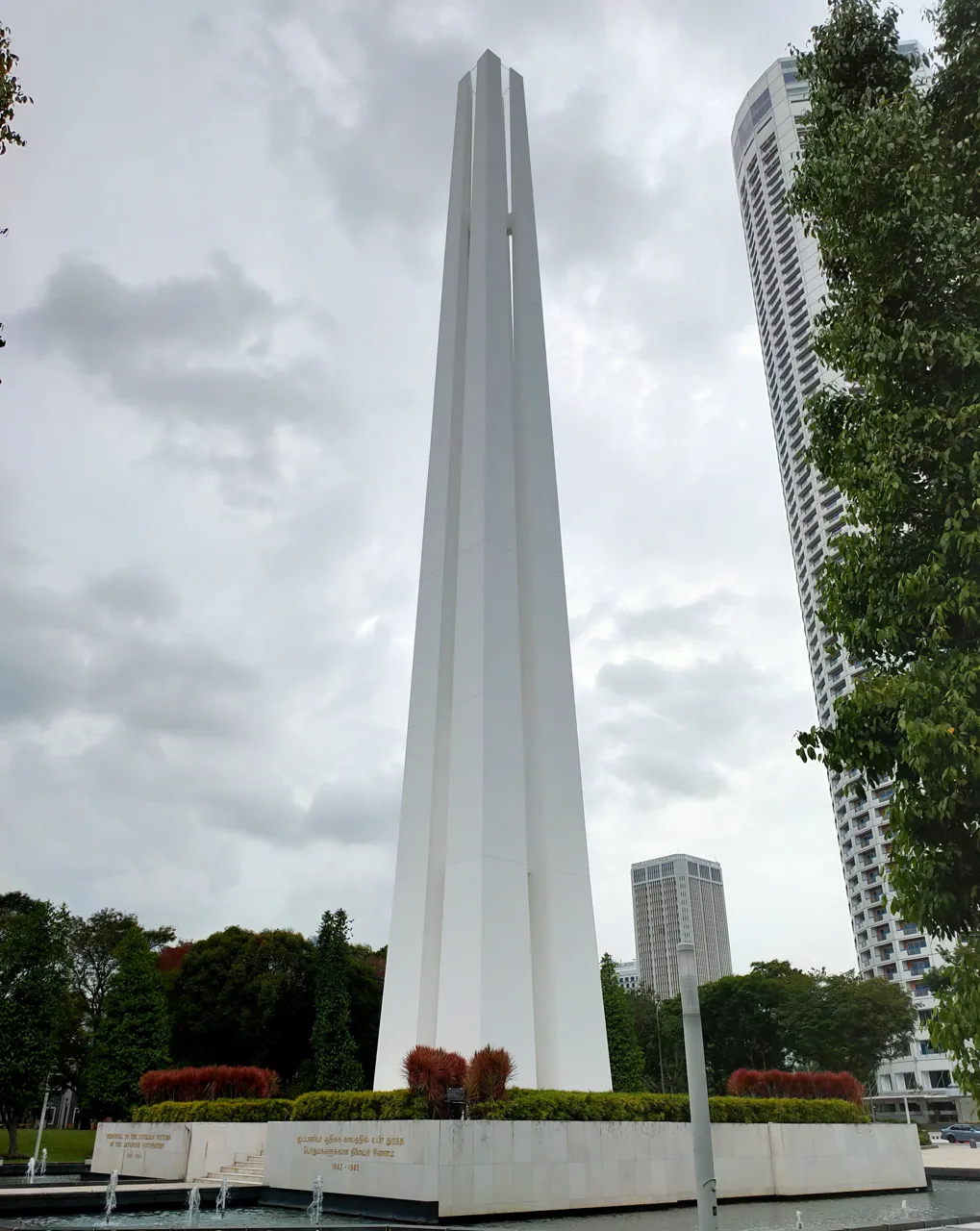 Four tall white columns rising together into the sky above a pool and low planting