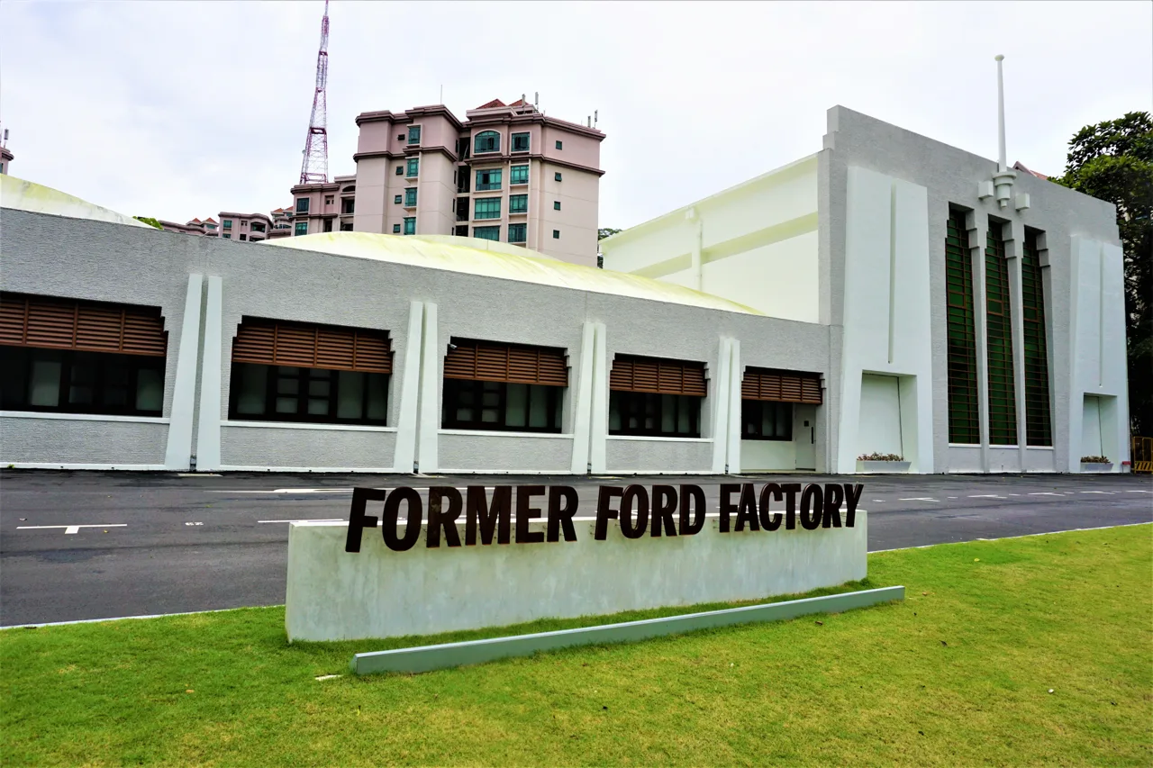 A white building with its name in heavy dark lettering on a low wall in front, and a lawn beyond
