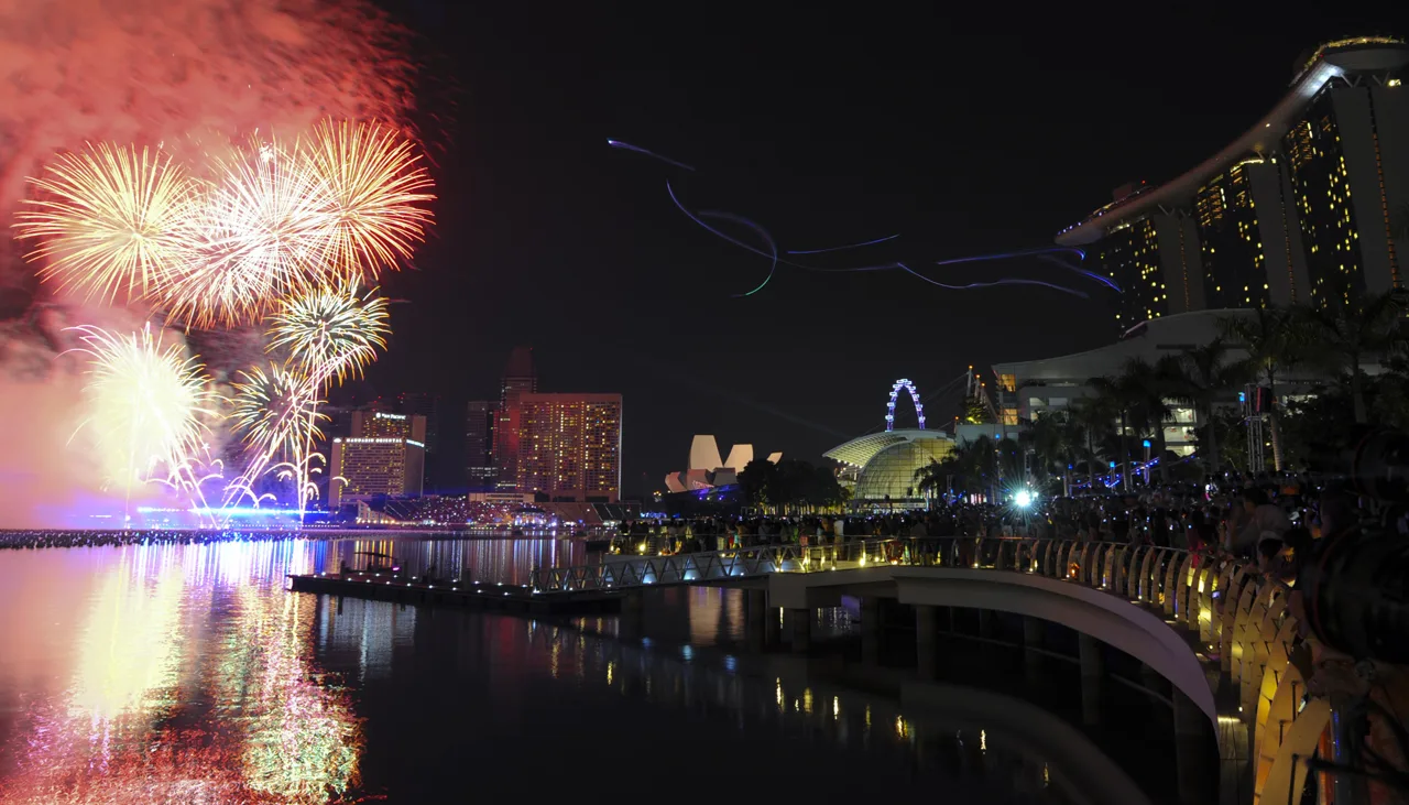Fireworks in the sky over Marina Bay, with Marina Bay Sands, the ArtScience Museum and the Singapore Flyer across the water, reflections on the bay and the waterfront promenade.